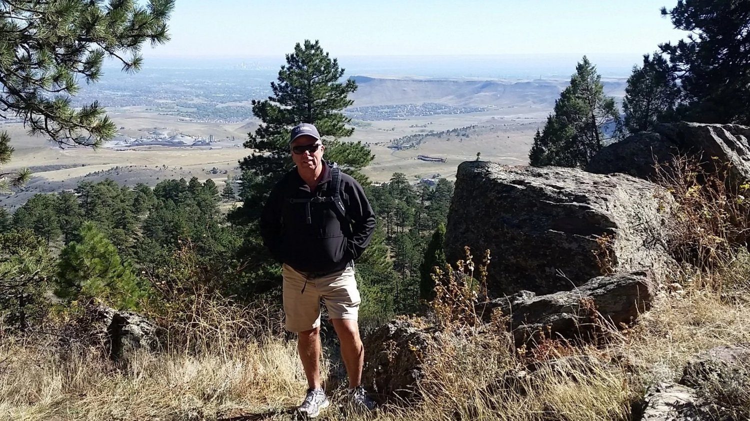 A man standing at a rocky overlook above a wide valley