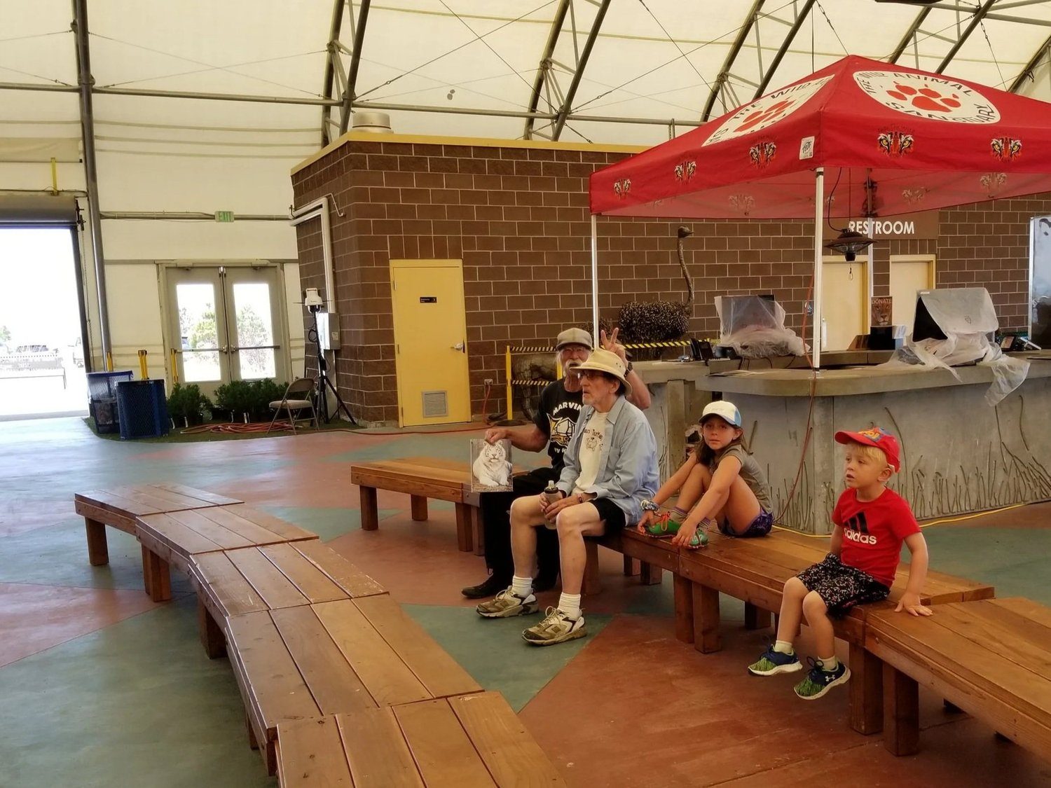 Kids and adults resting on benches in a covered pavilion