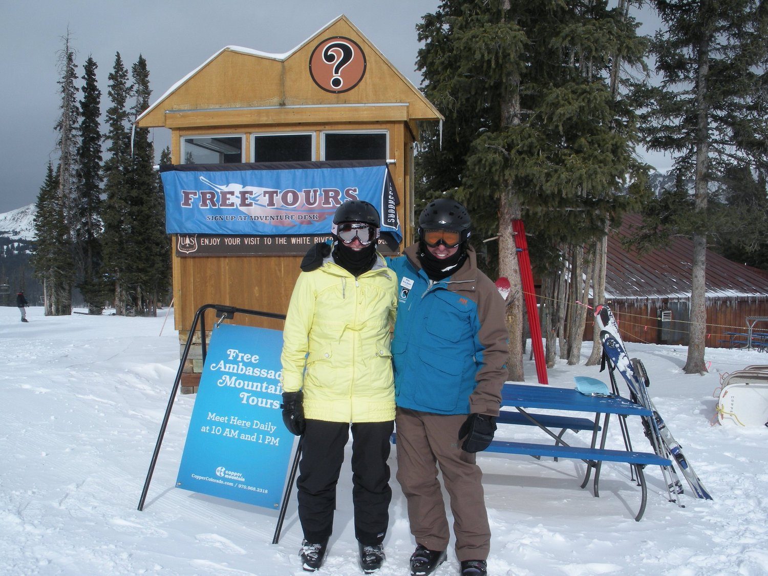 Two skiers beside a mountain tours sign